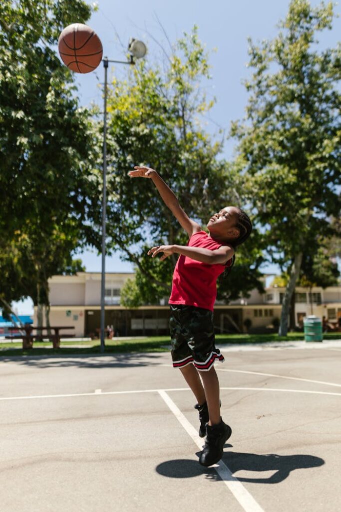 A young boy energetically shoots a basketball on a sunny outdoor court.